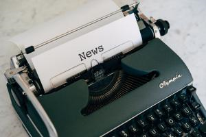 A photograph of a black typewriter, which has typed the word 'News' onto a sheet of paper.
